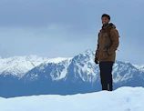 Man wearing a rugged Columbia jacket standing on a snowy mountain peak at sunrise.