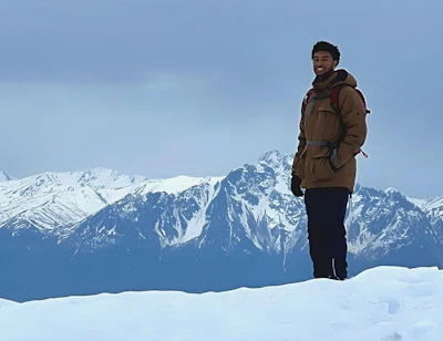 Man wearing a rugged Columbia jacket standing on a snowy mountain peak at sunrise.