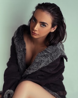 Elegant shot of a model seated, showcasing a timeless coat with soft natural lighting.