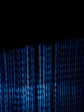 Vertical blue digital lines resembling binary code or data streams on a dark background create a visually striking and abstract pattern.
