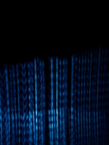 Vertical blue digital lines resembling binary code or data streams on a dark background create a visually striking and abstract pattern.