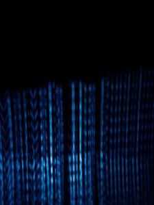 Vertical blue digital lines resembling binary code or data streams on a dark background create a visually striking and abstract pattern.