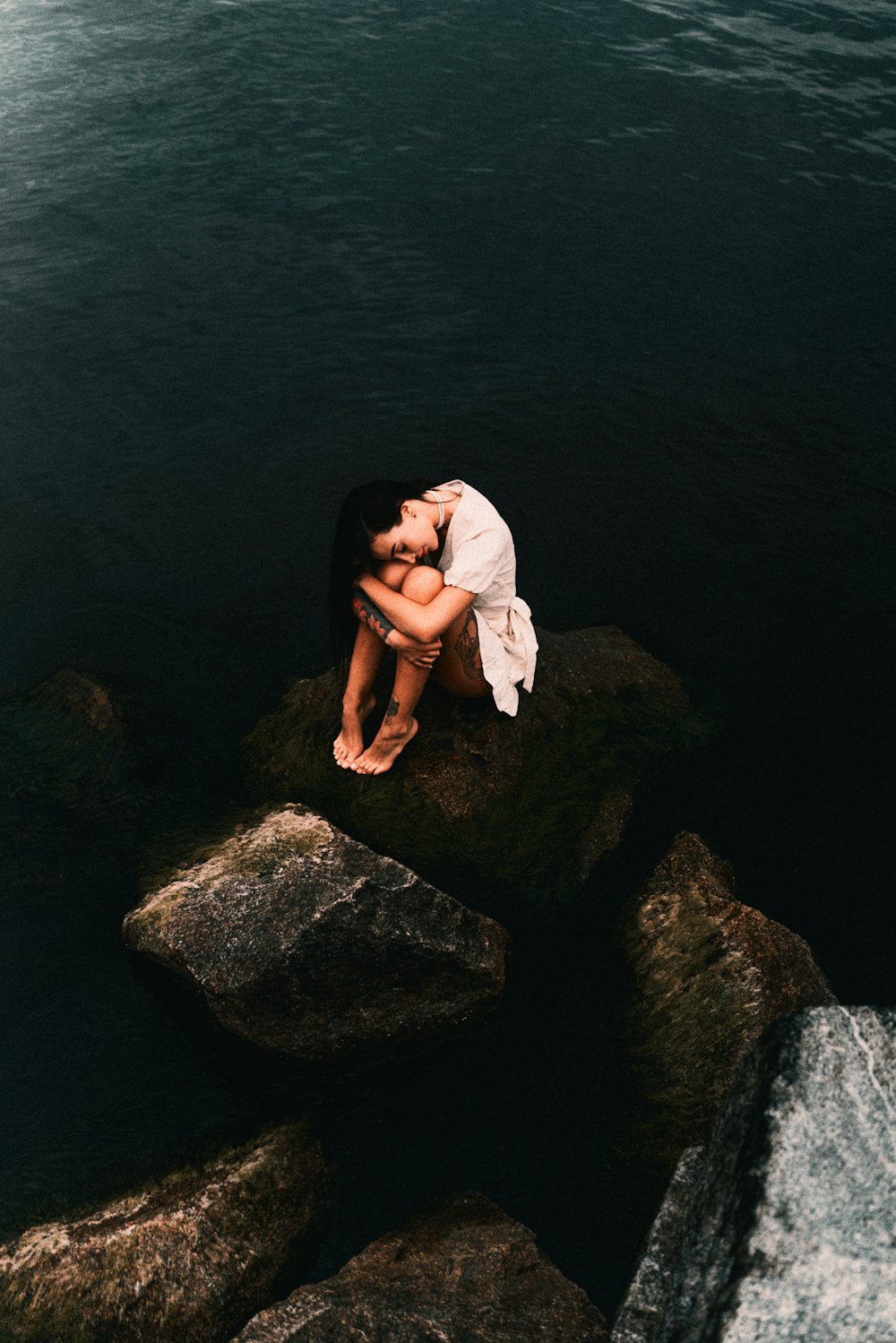 a woman is sitting on a rock by the water