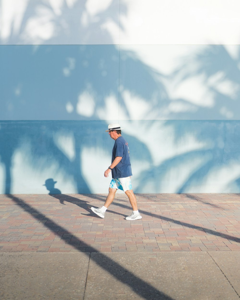 a man walking down a sidewalk next to a palm tree