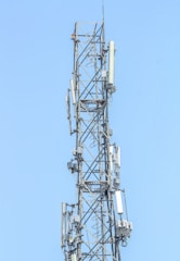 A tall metal communication tower with various antennas and equipment installed on it against a clear blue sky.