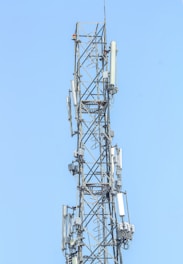 A tall metal communication tower with various antennas and equipment installed on it against a clear blue sky.
