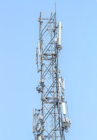 Technicians performing maintenance on a communication tower against a clear blue sky.