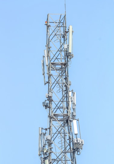 A technician inspecting a cell tower against a clear blue sky.