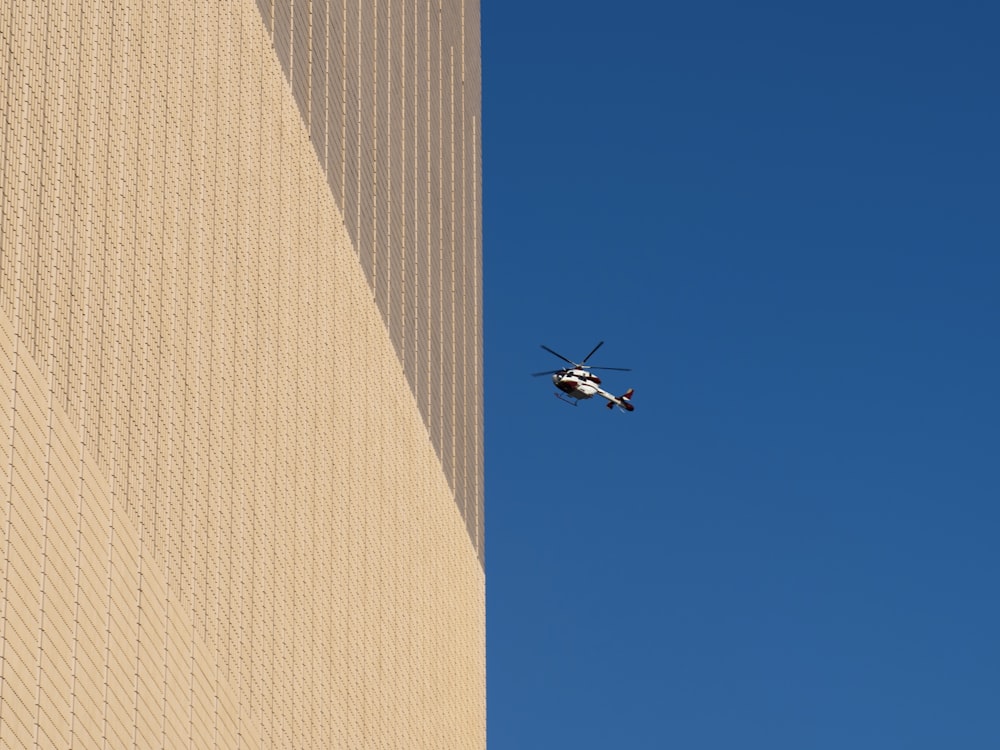 a helicopter flying over a tall building with a sky background