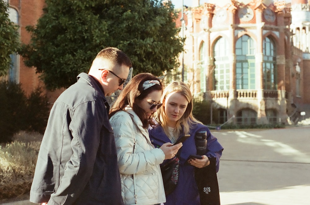 a group of people standing on a sidewalk looking at a cell phone