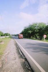 a red bus driving down a road next to a lush green field