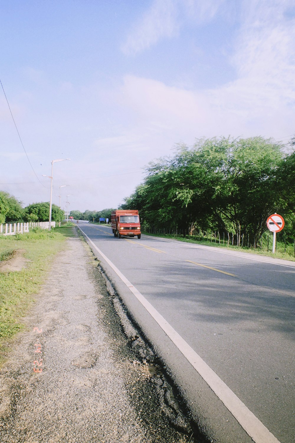 a red bus driving down a road next to a lush green field