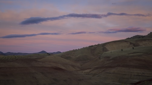 A wide landscape of rolling hills under a soft pastel sunset sky.