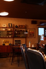 A cozy vintage-themed cafe featuring wooden shelves with various decorative items, including artwork and pottery. Retro signs labeled ‘KAFFE’ and ‘KARSK’ are displayed. A person is seated at a table, using a smartphone, with dim lighting contributing to the warm ambiance.