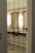 A bathroom interior featuring two sinks with ornate mirrors framed in gold. Wall-mounted lights are positioned vertically beside each mirror. The walls are covered in white tiles, and the floor has a patterned mosaic design. Plumbing and paper towel holders are visible under the sinks.