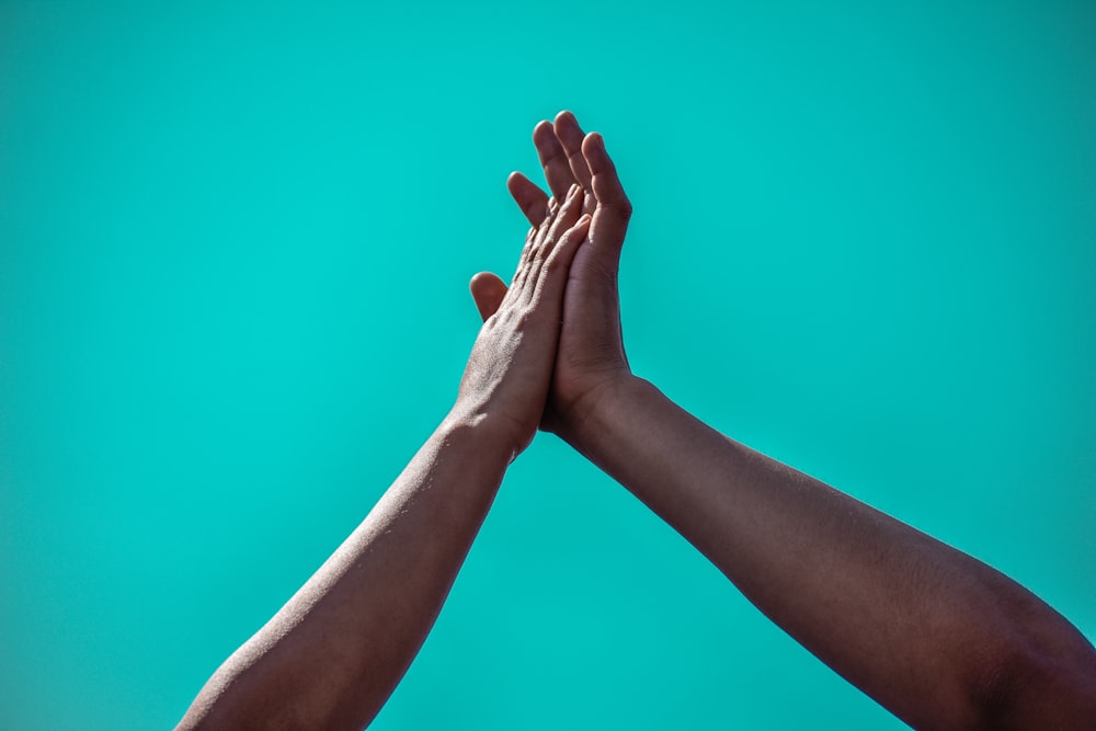 two hands reaching up into the air against a blue background