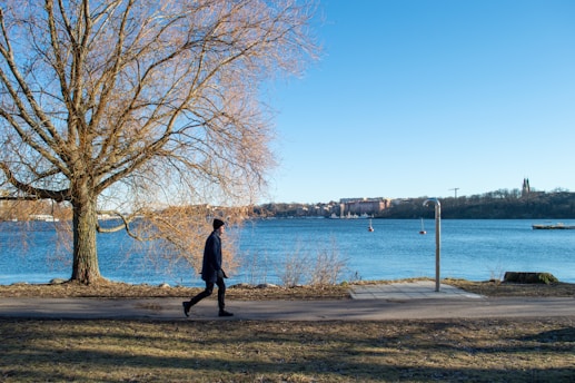 a man walking down a sidewalk next to a tree