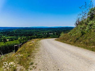 A freshly graded gravel driveway bordered by green grass under a bright blue sky.