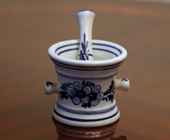 A decorative ceramic mortar and pestle set featuring blue floral patterns and stripes. The design is intricate and traditional, giving a vintage appeal.