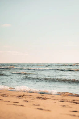 A serene ocean wave gently rolling onto a sandy shore under a clear sky