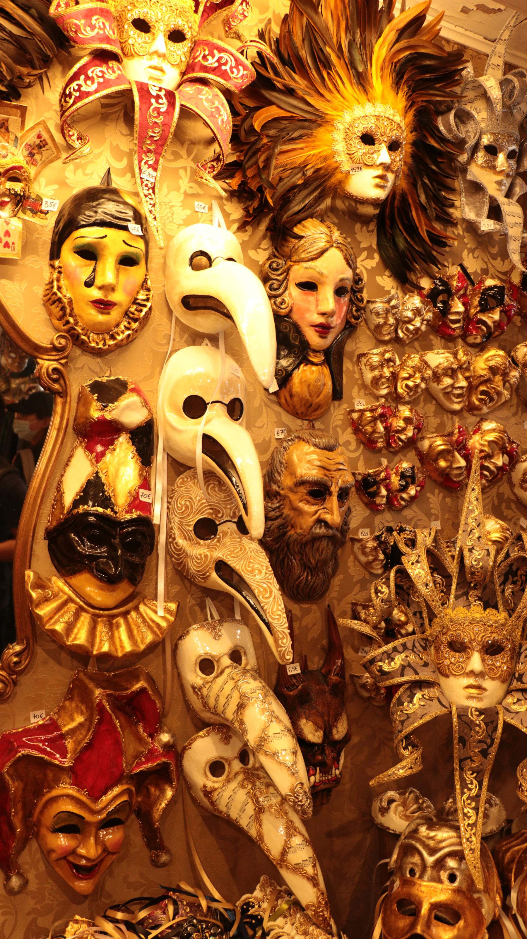 A shop wall crowded with Venetian carnival masks: long-nosed doctors, jesters and feathered faces