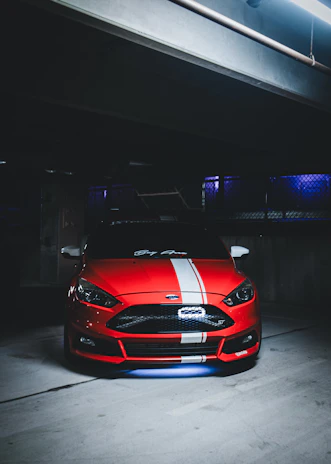 A high-performance car lifted in the garage, ready for detailed inspection beneath sharp race red lighting.