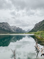 A calm mountain lake reflecting rugged peaks under a cloudy sky.