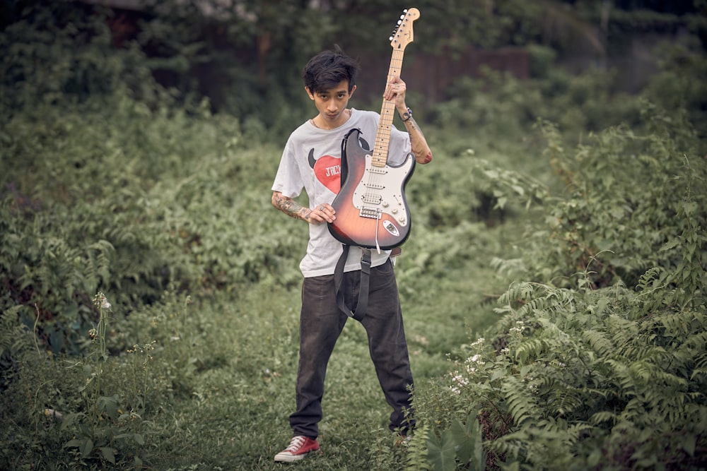 a young man holding a guitar in a field