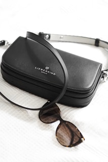 A sleek black leather handbag with a strap lies alongside a pair of tortoiseshell sunglasses. The handbag features the brand name 'Liebeskind Berlin' printed in white on the front.