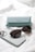 A light blue Tiffany & Co. glasses case is placed on a white textured surface, accompanied by a pair of dark sunglasses and a smartphone with a light-colored case.