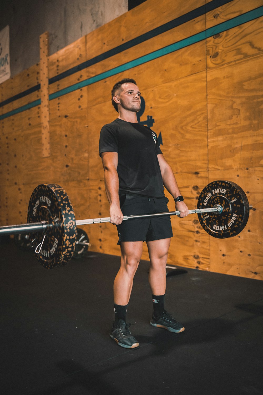a man holding a barbell in front of a wooden wall