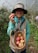 A smiling farmer standing in a lush tropical orchard holding fresh fruit.