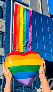 A warm, pastel rainbow-colored hand gently holding a heart symbol, representing inclusion and care.