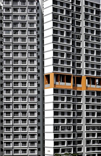 Tall residential buildings with uniform, repetitive window patterns create a modern urban landscape. The structures have a predominantly white and gray facade with a distinct orange section near the top, adding a splash of color.