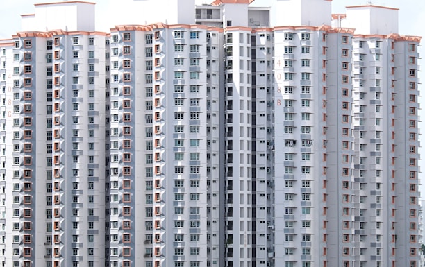 A cluster of tall residential buildings with numerous windows and balconies. The structures are modern, with a uniform design featuring light-colored exteriors and orange decorative elements. There appear to be laundry items hanging on some of the balconies, indicating occupancy.