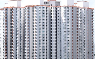 A cluster of tall residential buildings with numerous windows and balconies. The structures are modern, with a uniform design featuring light-colored exteriors and orange decorative elements. There appear to be laundry items hanging on some of the balconies, indicating occupancy.