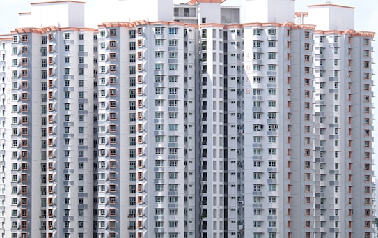 A cluster of tall residential buildings with numerous windows and balconies. The structures are modern, with a uniform design featuring light-colored exteriors and orange decorative elements. There appear to be laundry items hanging on some of the balconies, indicating occupancy.
