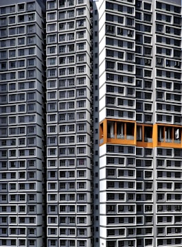 Tall residential buildings with a modern architectural design, featuring numerous windows arranged in an orderly, repetitive pattern. Some sections are highlighted with orange accents.