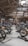 A motorcycle exhibition features several vintage-style bikes displayed inside a wooden-roofed hall. People are casually walking around, observing the motorcycles. The setting includes banners and signage for Devitt Insurance. The atmosphere is well-lit, highlighting the classic design and detailing of the bikes.