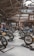 A motorcycle exhibition features several vintage-style bikes displayed inside a wooden-roofed hall. People are casually walking around, observing the motorcycles. The setting includes banners and signage for Devitt Insurance. The atmosphere is well-lit, highlighting the classic design and detailing of the bikes.