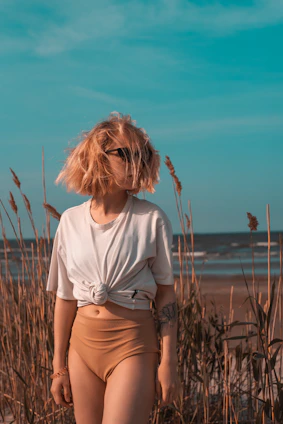 a woman standing on a beach next to tall grass