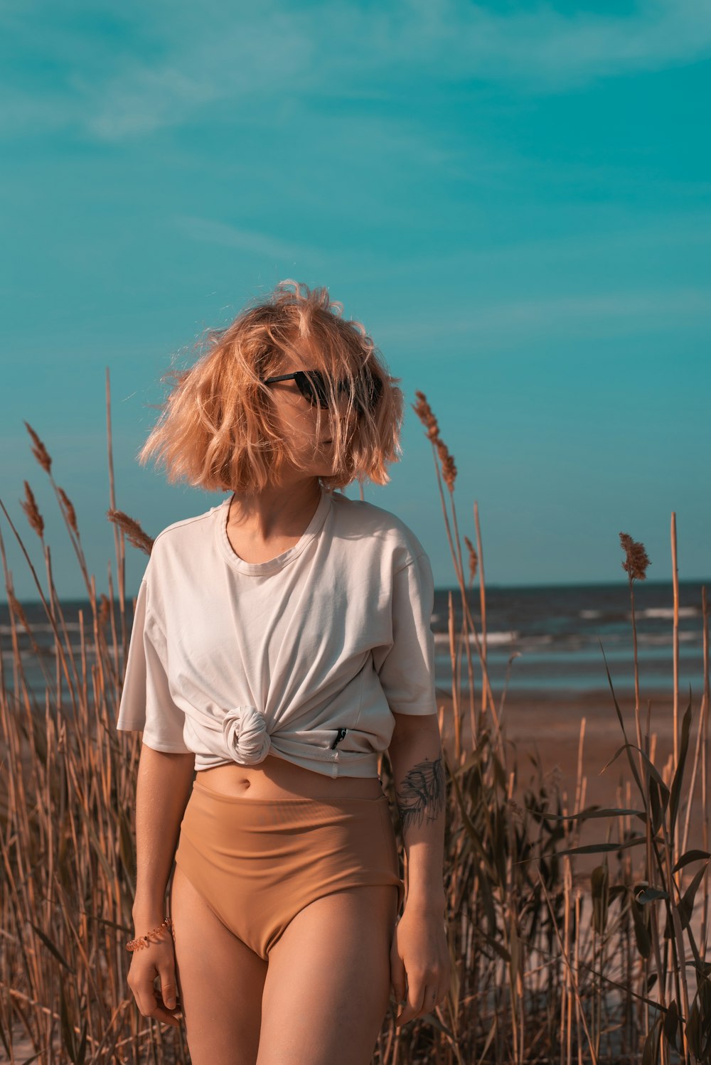 a woman standing on a beach next to tall grass