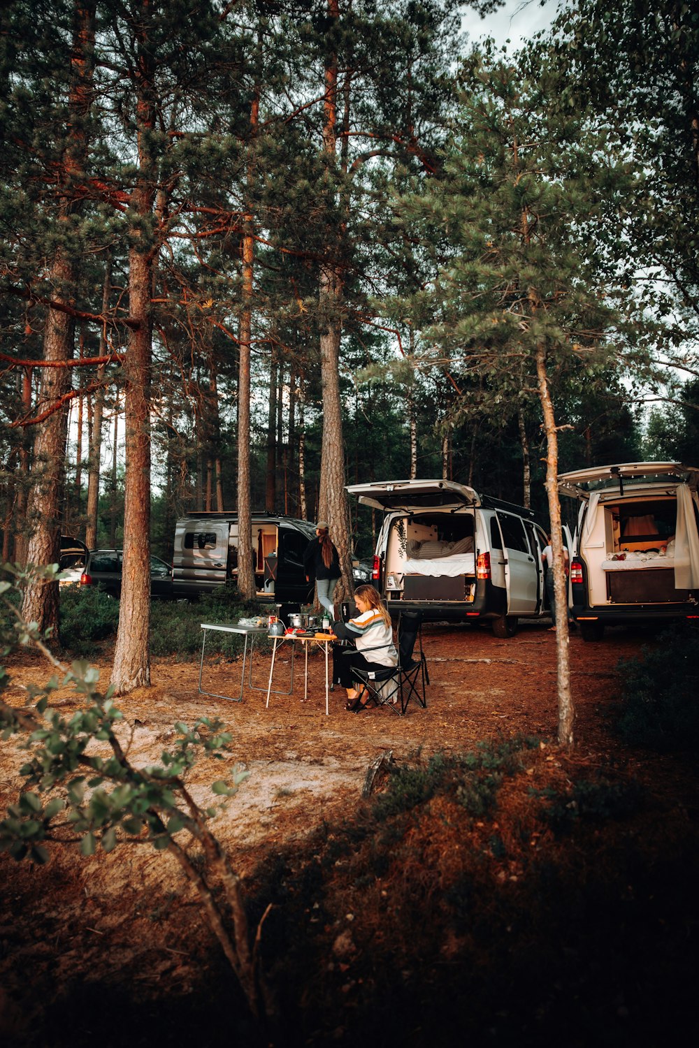 a group of people sitting around a camper in the woods