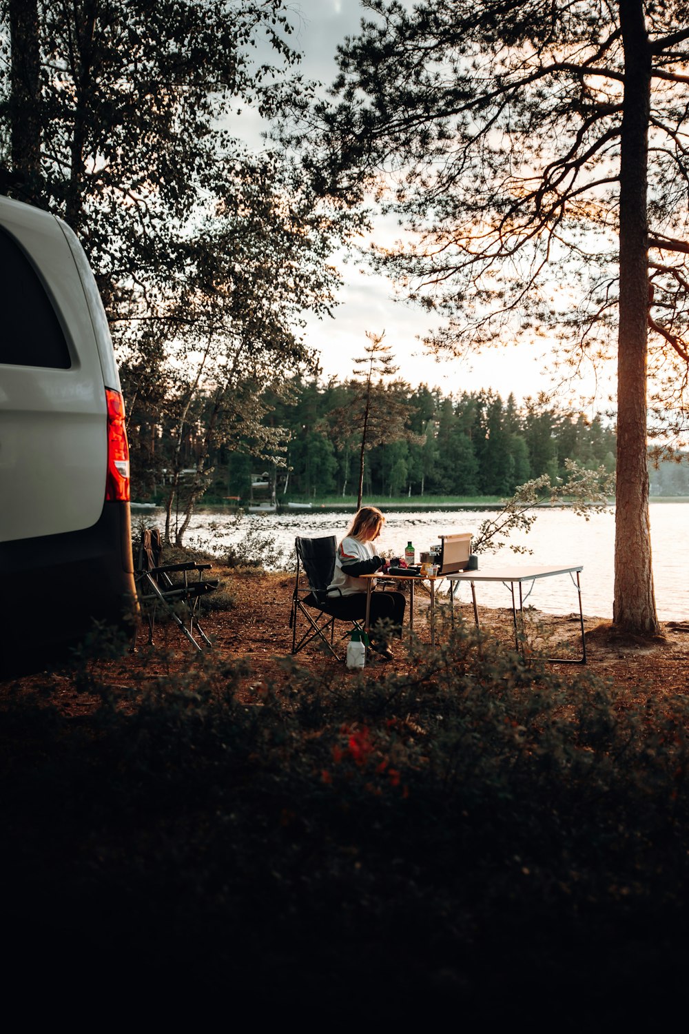 Una furgoneta estacionada junto a un lago con una persona sentada en una mesa