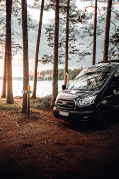 A rugged van nestled in a forest clearing with a male adventurer standing nearby, mountain peaks bathed in warm evening light.