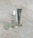 A collection of skincare products displayed on a light speckled surface. The items include a small bottle of micellar water, a tube labeled 'PEEL' for a brightening AHA peel mask, a green jade gua sha tool, and a gold massage tool with two spherical ends.