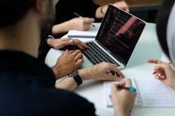 a group of people sitting around a laptop computer
