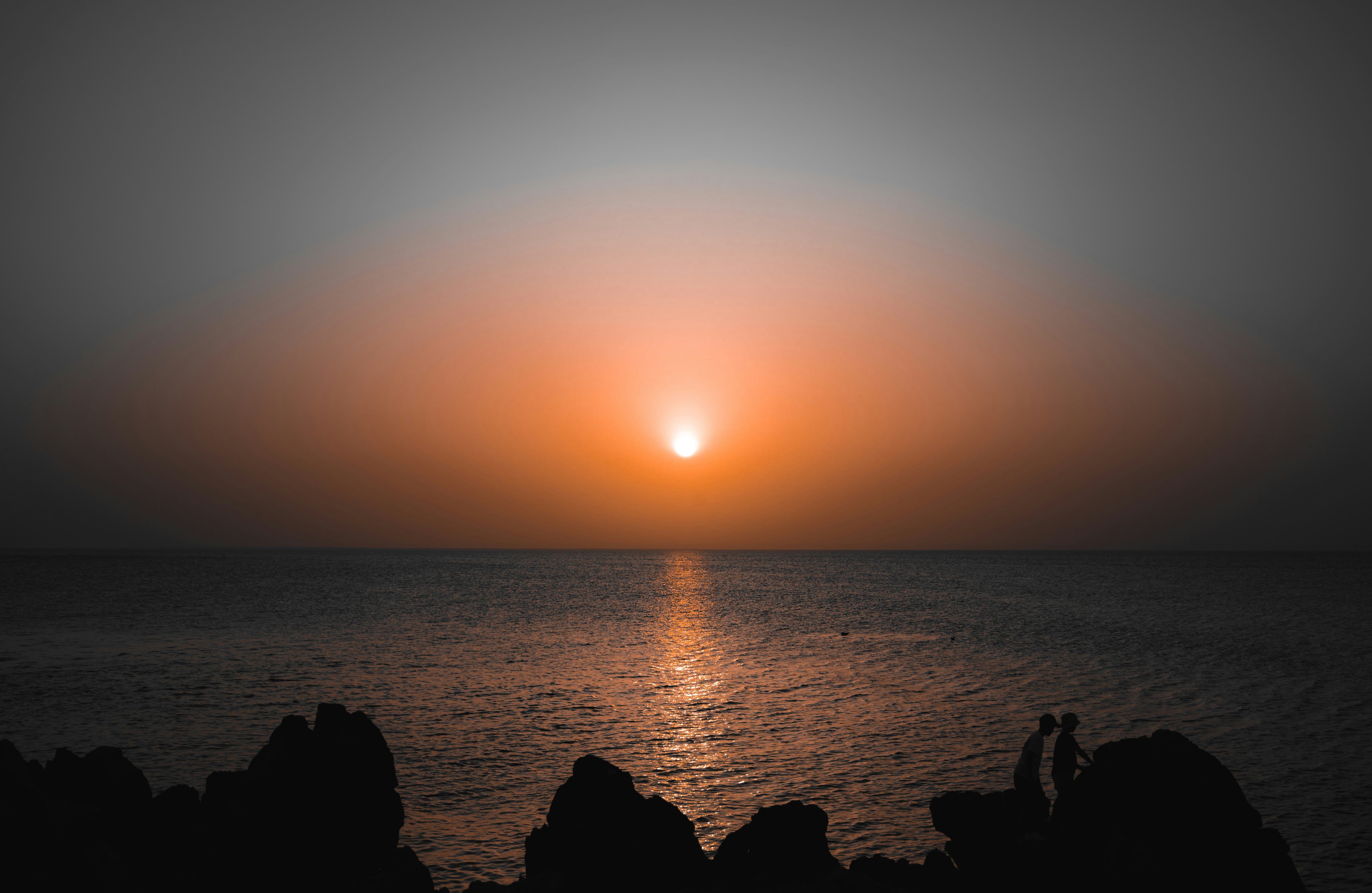 the sun is setting over the ocean with rocks in the foreground