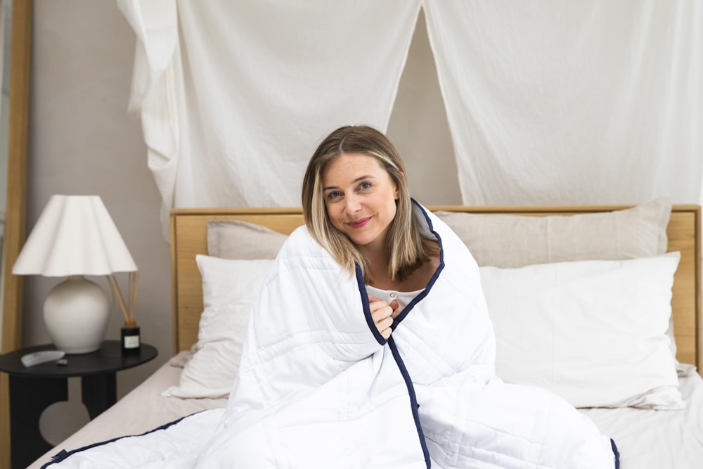 a woman sitting on a bed wrapped in a blanket