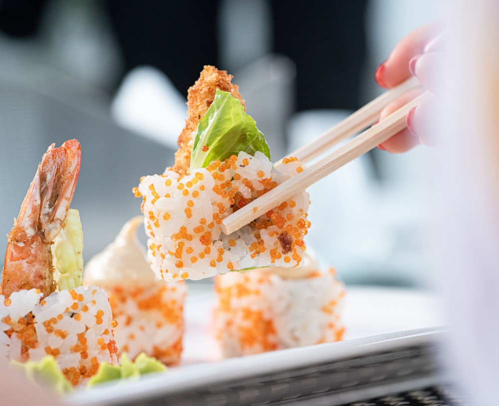 a person holding chopsticks over a plate of sushi